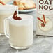 A glass mug with Elmhurst Milked Oat Nog in it, topped with cinnamon and nutmeg.