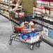 A man pushing a black Regency Supermarket shopping cart filled with groceries.