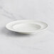 A RAK Porcelain ivory deep plate with an embossed rim on a marble surface.