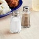 A Choice salt shaker with a mushroom top next to a plate of mashed potatoes on a table.