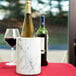 A Tablecraft white marble wine cooler holding a wine bottle and glass on a table.