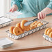 A woman using a spatula to put doughnuts into a rectangular wire basket filled with pastries.