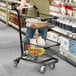 A man pushing a Regency black two-tier shopping cart full of food.