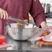 A person using tongs to put meat in a Choice stainless steel mixing bowl.