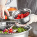 A gloved hand holding a Choice stainless steel mixing bowl filled with tomatoes.