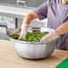 A person in gloves mixing greens in a Choice stainless steel mixing bowl.