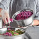 A woman in a chef's uniform holding a bowl of shredded red cabbage in a Choice stainless steel mixing bowl with a silicone bottom.