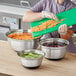 A woman using a Choice stainless steel mixing bowl to cut cucumbers on a green cutting board.