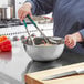 A woman mixing food in a Choice stainless steel mixing bowl.