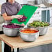 A woman in a kitchen using a Choice stainless steel mixing bowl to prepare vegetables.