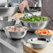 A person using tongs to mix shredded vegetables in a Choice stainless steel mixing bowl.