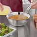 A hand pouring liquid from a bottle into a stainless steel mixing bowl.