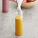 A hand pouring yellow liquid into an 8 oz. PET Cosmo Bullet Bottle.