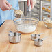 A person mixing oats and flour in a bowl with Tablecraft measuring cups and a whisk.