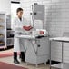A woman in a white coat using a ProCut vertical band meat saw to cut meat.