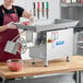A woman in an apron using a ProCut #32 electric meat grinder on a counter in a butcher shop to grind meat.