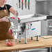 A woman in a brown apron uses a ProCut electric meat grinder on a counter.