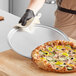 A person cleaning a round metal surface with a pizza on it.