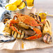 A Chesapeake blue crab on a plate of corn, potatoes, and lemons with a nutcracker and a bucket of lemons.