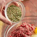 A hand mixing ground meat with Regal Meatloaf Seasoning in a bowl.