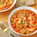 A bowl of soup with shrimp, rice, and vegetables next to a fork.