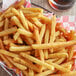 A basket of french fries on a table with a glass of beer.