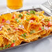 A plate of nachos with GOOD PLANeT vegan cheddar cheese and tomatoes on a table.