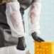 A person wearing white Malt Impact polyethylene sleeves holding a white plastic container.