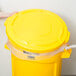 A person's hand placing a yellow Rubbermaid trash can lid over a yellow Rubbermaid trash can.