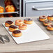 A tray of doughnuts on a white corrugated half sheet cake board in a bakery display.