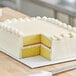 A white sheet cake with a slice cut out on a white double-wall corrugated cake pad.