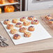 A tray of pastries on a white corrugated half sheet cake board on a table in a bakery display.