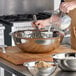 A person pouring milk into a Vollrath stainless steel mixing bowl.