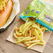 A hot dog with Sea Salted Veggie Stix and french fries on a table in a stadium concession stand.