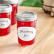 A pack of Avery oval labels on jars of strawberry jam on a table.