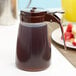 A Tablecraft brown polypropylene syrup dispenser with a handle.