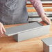 A person holding a loaf of bread in a silver rectangular metal Baker's Mark loaf pan.