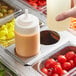 A person using a Choice stainless steel squeeze bottle holder to pour sauce into a container of food on a counter.