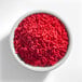 A white bowl filled with red sprinkles.