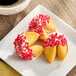 A plate of fortune cookies dipped in white icing and decorated with red sprinkles.