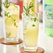 A close-up of two glasses of lemonade with rosemary and lemon on a table.