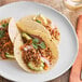 A white plate with tacos made with Bob's Red Mill Textured Vegetable Protein and topped with avocado and onions.