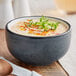 An Acopa Embers midnight blue stoneware bowl filled with soup and green sprouts.