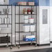 A black epoxy 5-shelf storage rack with casters, holding various kitchen supplies and containers.