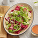 An Acopa Harvest Tan matte coupe stoneware platter with salad on a table.