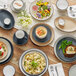 A white Acopa stoneware mug with a black rim on a table with plates of food and utensils.