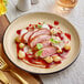 An Acopa Harvest Tan Matte coupe stoneware plate with food on it on a table.