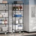 A Steelton black metal wire shelving unit with shelves and casters holding food items.