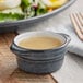 A Midnight Blue matte stoneware sauce cup filled with liquid on a table next to a plate of salad.