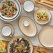 A table set with Acopa Harvest Tan Matte Coupe Stoneware platters, bowls, and cups of food.